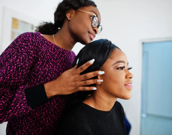 African American woman applying make-up by make-up artist at beauty saloon.