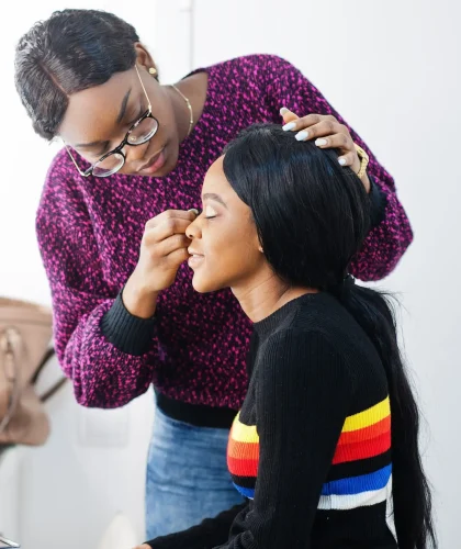 African American woman applying make-up by make-up artist at beauty saloon.